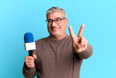 Photo for Middle age senior man smiling and looking happy, gesturing victory or peace. journalist or tv presenter with a micro - Royalty Free Image