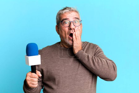 Foto de Hombre mayor de mediana edad sintiéndose sorprendido y asustado. periodista o presentador de televisión con un micro - Imagen libre de derechos