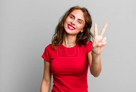 Photo for Young pretty woman smiling and looking friendly, showing number two or second with hand forward, counting down - Royalty Free Image