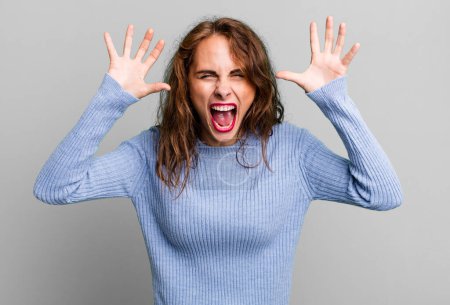 Photo for Young pretty woman screaming in panic or anger, shocked, terrified or furious, with hands next to head - Royalty Free Image