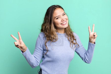 Photo for Young pretty woman smiling and looking happy, friendly and satisfied, gesturing victory or peace with both hands - Royalty Free Image