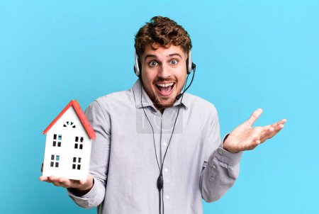 Photo for Young adult caucasian man. real state agent with headset and a house model - Royalty Free Image