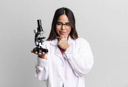 Photo for Hispanic pretty woman smiling with a happy, confident expression with hand on chin. scients student with a microscope - Royalty Free Image