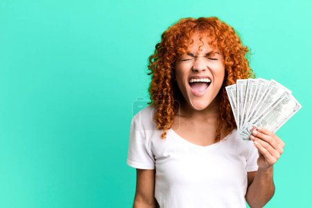 Photo for Red hair pretty woman shouting aggressively, looking very angry. dollar banknotes and money concept - Royalty Free Image