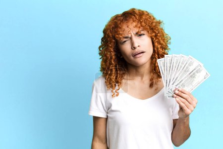 Photo for Red hair pretty woman feeling puzzled and confused. dollar banknotes and money concept - Royalty Free Image