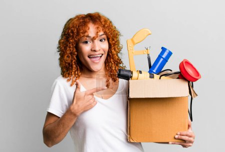 Photo for Red hair pretty woman looking excited and surprised pointing to the side. housekeeper and toolbox concept - Royalty Free Image