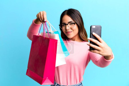 Téléchargez les photos : Hispanic pretty young adult woman with shopping bags and her smartphone. buy concept - en image libre de droit