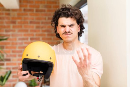 Téléchargez les photos : Jeune homme beau tenant un casque de moto à l'intérieur de la maison - en image libre de droit