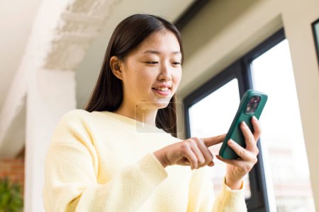 Téléchargez les photos : Asian pretty woman using a smartphone in a cool home - en image libre de droit