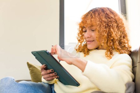 Téléchargez les photos : Young red hair latin pretty woman using a touchscreen pad at home - en image libre de droit