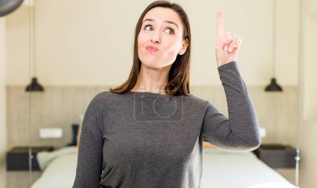 Photo for Young adult pretty woman feeling like a genius holding finger proudly up in the air after realizing a great idea, saying eureka - Royalty Free Image