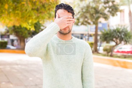 Photo for Young hispanic man covering eyes with one hand feeling scared or anxious, wondering or blindly waiting for a surprise - Royalty Free Image