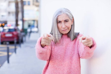 Téléchargez les photos : Senior retraité jolie femme aux cheveux blancs pointant vers l'avant à la caméra avec les deux doigts et l'expression en colère, vous disant de faire votre devoir - en image libre de droit