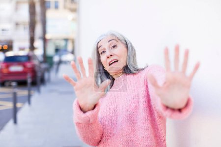 Foto de Jubilada bastante mujer de pelo blanco sintiéndose aterrorizada, retrocediendo y gritando de horror y pánico, reaccionando a una pesadilla - Imagen libre de derechos
