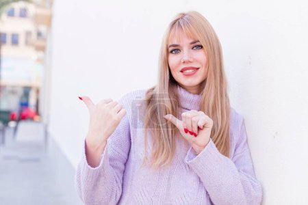 Photo for Young pretty woman smiling cheerfully and casually pointing to copy space on the side, feeling happy and satisfied - Royalty Free Image