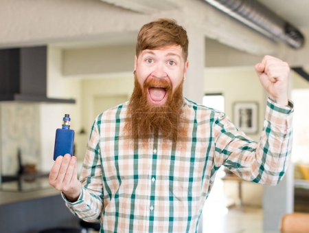 Foto de Hombre de pelo rojo sintiéndose sorprendido, riendo y celebrando el éxito con un vaper - Imagen libre de derechos