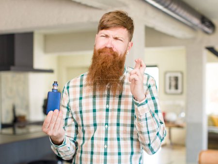 Photo for Red hair man crossing fingers and hoping for good luck with a vaper - Royalty Free Image