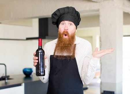 Photo for Red hair man shrugging, feeling confused and uncertain with a wine bottle. chef concept - Royalty Free Image
