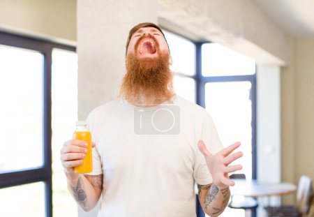 Photo for Red hair man screaming with hands up in the air with an orange juice bottle - Royalty Free Image