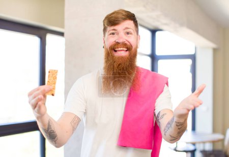 Photo for Red hair man smiling happily and offering or showing a concept with a cereal bar. fitness concept - Royalty Free Image