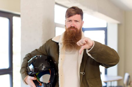 Photo for Red hair man feeling cross,showing thumbs down with a motorbike helmet - Royalty Free Image