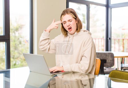 Photo for Pretty caucasian woman looking unhappy and stressed, suicide gesture making gun sign with hand, pointing to head. home interior concept - Royalty Free Image