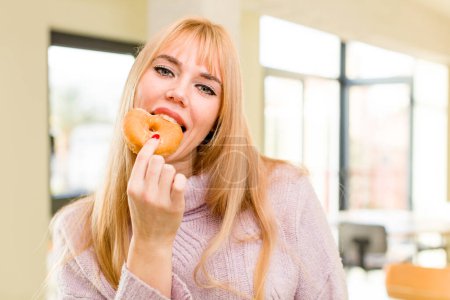Foto de Una mujer joven y bonita con una rosquilla. concepto de dieta poco saludable en el interior del hogar - Imagen libre de derechos