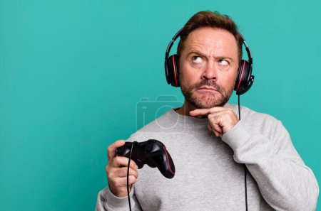 Photo for Middle age man thinking, feeling doubtful and confused. gamer concept with a control and headset - Royalty Free Image