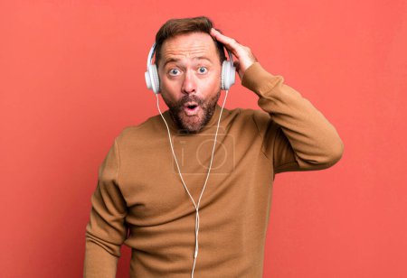 Téléchargez les photos : Homme d'âge moyen l'air heureux, étonné et surpris. écouter de la musique avec un casque - en image libre de droit