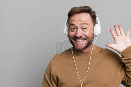 Téléchargez les photos : Homme d'âge moyen souriant et l'air amical, montrant le numéro cinq. écouter de la musique avec un casque - en image libre de droit