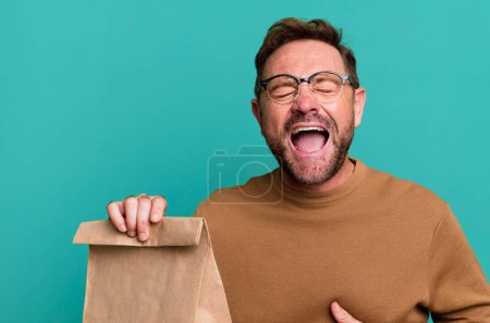 Foto de Un hombre de mediana edad riéndose en voz alta ante una broma graciosa. llevar bolsa de papel - Imagen libre de derechos
