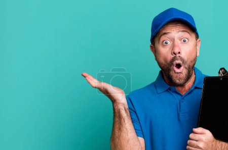 Foto de Hombre de mediana edad que parece sorprendido y sorprendido, con la mandíbula caída sosteniendo un objeto. empleado de la empresa con un inventario - Imagen libre de derechos