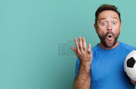 Photo for Middle age man amazed, shocked and astonished with an unbelievable surprise. with a soccer ball. fitness concept - Royalty Free Image
