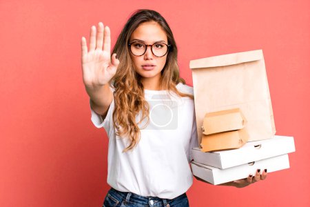 Photo for Hispanic pretty woman looking serious showing open palm making stop gesture. with fast food packages - Royalty Free Image