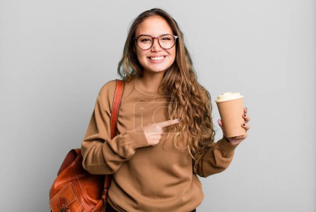 Téléchargez les photos : Hispanique jolie femme souriant joyeusement, se sentant heureux et pointant vers le côté. concept de café à emporter - en image libre de droit