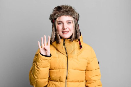 Téléchargez les photos : Jeune jolie femme souriante et sympathique, montrant le numéro quatre. concept froid et manteau - en image libre de droit