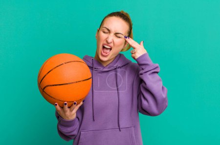 Foto de Joven bonita mujer buscando infeliz y estresado, gesto suicida haciendo señal de arma. concepto de baloncesto - Imagen libre de derechos