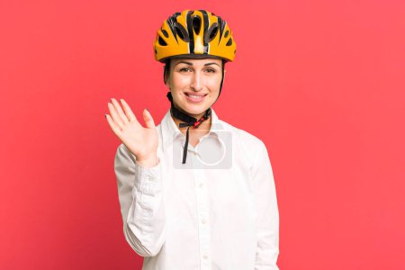 Foto de Joven bonita mujer sonriendo felizmente, saludándote con la mano, dándote la bienvenida y saludándote. concepto de negocio y bicicleta - Imagen libre de derechos