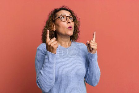 Photo for Middle age hispanic woman feeling awed and open mouthed pointing upwards with a shocked and surprised look - Royalty Free Image