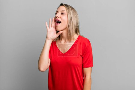 Photo for Blonde adult woman profile view, looking happy and excited, shouting and calling to copy space on the side - Royalty Free Image