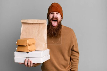 Foto de Joven adulto pelo rojo barbudo hombre fresco con una bolsa de papel con comida para llevar - Imagen libre de derechos