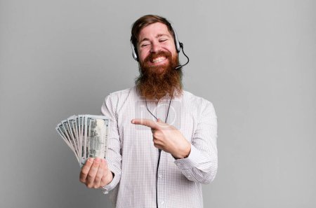 Foto de Joven adulto pelo rojo barbudo agente fresco hombre con auriculares y billetes de dólar - Imagen libre de derechos