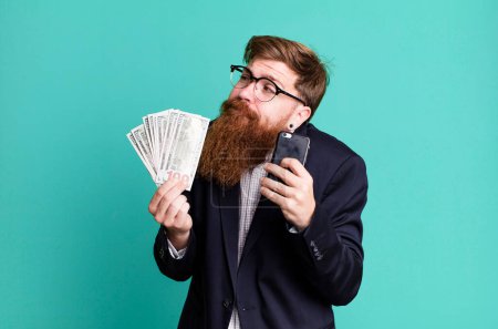 Téléchargez les photos : Jeune adulte cheveux roux barbu homme d'affaires cool avec des factures et un téléphone - en image libre de droit
