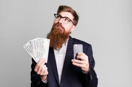 Téléchargez les photos : Jeune adulte cheveux roux barbu homme d'affaires cool avec des factures et un téléphone - en image libre de droit