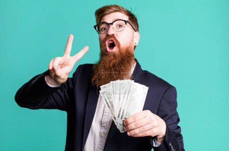 Téléchargez les photos : Jeune adulte cheveux roux barbu cool homme d'affaires avec des billets de banque - en image libre de droit