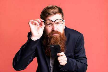 Foto de Joven adulto pelo rojo barbudo fresco hombre de negocios utilizando su teléfono inteligente - Imagen libre de derechos