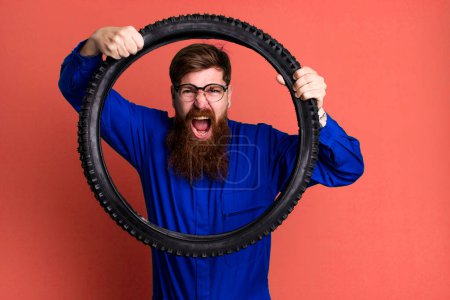 Téléchargez les photos : Jeune adulte cheveux roux barbu cool réparation homme avec une roue de vélo - en image libre de droit