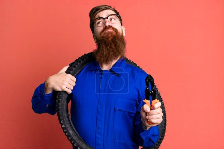 Foto de Joven adulto pelo rojo barbudo fresco reparación hombre con una rueda de bicicleta - Imagen libre de derechos