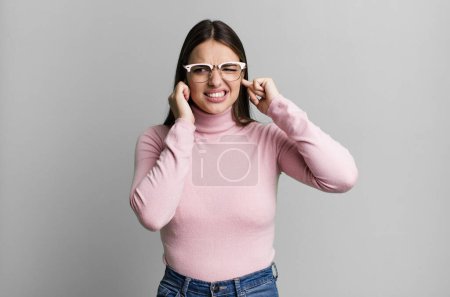 Téléchargez les photos : Pretty young adult woman looking angry, stressed and annoyed, covering both ears to a deafening noise, sound or loud music - en image libre de droit