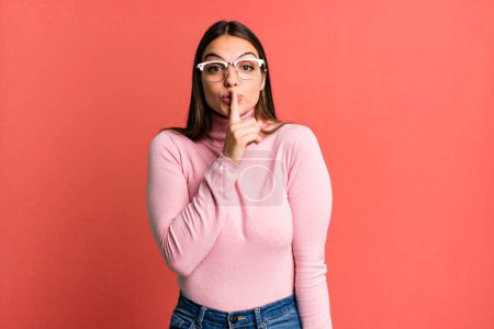 Photo for Pretty young adult woman asking for silence and quiet, gesturing with finger in front of mouth, saying shh or keeping a secret - Royalty Free Image